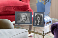 Coloured enamel photo frames displaying a happy girl and a dog on a stylish table in a cozy living room setting.