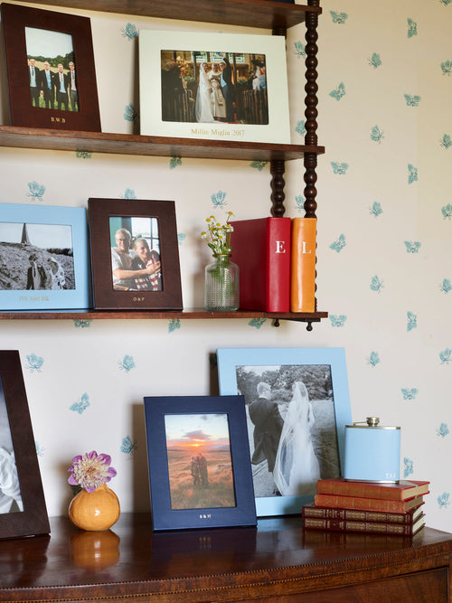 Chelsea Landscape Leather Photo Frame 7x5 displayed on a wooden shelf with various photos and decorative items.