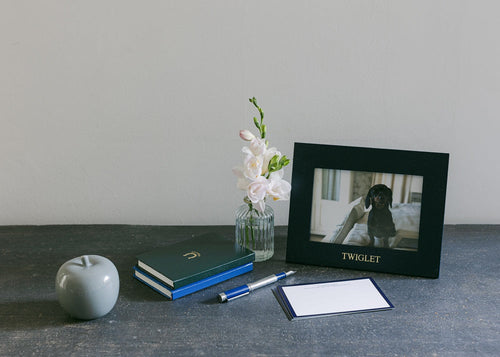 Jubilee landscape photograph frame displaying a pet photo with stationery, a decorative apple, and flowers on a modern table.
